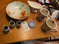 Overview photo showing all items on wooden table including Homer Laughlin floral bowl, mugs, egg cups, gravy boat, and Wedgwood plate.