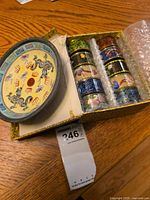 Boxed set showing ten cylindrical cloisonné napkin holders in multiple colors and designs alongside a small round bowl with dragons on the cover.