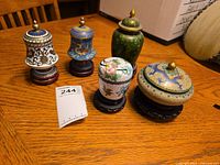 Five cloisonné lidded containers on wooden table, showing variety of colors and designs.