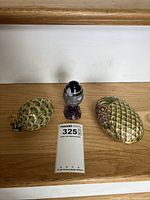 Three cloisonné items on wooden surface: pineapple ornament, collectible egg on stand, pineapple trinket dish