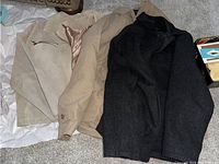 Three men's coats displayed on a surface including beige leather, beige London Fog, and dark gray wool coats, all size medium