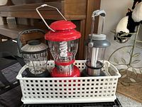 Three portable lanterns placed inside a white plastic storage basket visible on carpet near furniture.