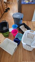All containers and baskets arranged on wooden floor showing variety and sizes including laundry baskets, bins, small buckets, and wheeled container.