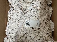 Photo showing folded crocheted tablecloth with handmade circular crochet patterns and a label with 'Rice' on it.