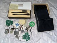 Lot layout showing two Cross Classic Black pens in original cream colored box with certificate, three black wallets, and five padlocks with keys and keychains on white paper.