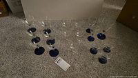 Photo showing various crystal glasses with blue bases, arranged on carpet.