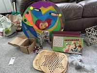 Gaming items displayed on carpet, including painted shield, Scrabble games, wooden bead track board games, small box of sports cards