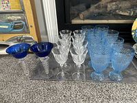 Full set of glassware including 2 cobalt blue martini glasses, 8 clear crystal wine glasses, and 8 blue iced tea glasses with hobnail pattern arranged on mat