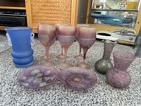 View showing full lot of 6 purple frosted wine glasses, 2 oval side plates with floral designs, and 2 vases (one blue with handles, one purple)