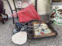 Photo showing large pink plastic tote behind two leather-like handbags and small white beaded bag on carpet near furniture.