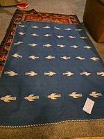 Full view of blue Navajo rug with repeating beige bird motifs displayed on floor