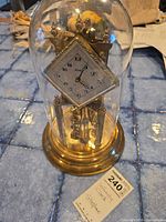 Front view of Kundo Infinity clock under glass dome on a blue tiled surface with a lot tag.