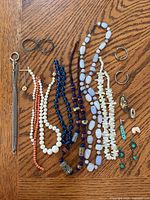 Top view of assorted beaded necklaces, various earrings, pins, and tie tack jewelry arranged on wooden surface.