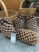 Four large pine cones arranged in front of three woven baskets with handles and one covered basket in background