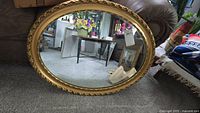 Full view of the large vintage round mirror on the carpet. Shows ornate gold wooden frame with floral carving detail. Reflects room and furniture.