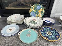 Various salad plates, a salad bowl, decorative platters appearing in a group on carpet, showing different brands and patterns