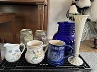 Photo of Lenox vase, cobalt blue pitcher, ceramic mugs, Wedgwood creamer and Ball jars arranged on a rack