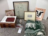 Wide view of all items including framed pictures, books, postcards, and woven blanket with Massachusetts town scenes on carpeted floor.