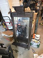 Full front view of large antique beveled mirror with carved wood frame and attached shelf in a cluttered storage area.