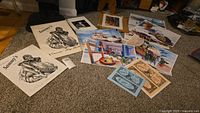 Wide shot of the assortment of art prints and vintage styled prints laid out on carpet showcasing variety of styles and subjects.