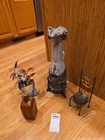 Photo showing four decor items: brown leather bottle, tall ceramic vase, metal flower decoration, and metal chair candle holder.