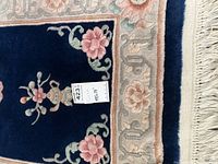 Close-up of rug's floral design and border showing pink flowers on dark blue background with fringed edge