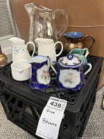 Photo of seven assorted pitchers and one sugar bowl displayed on a black crate with a dealer label visible.