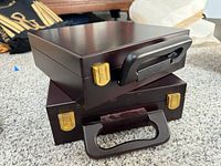 Two wooden poker set cases stacked on carpet, showing front handles and gold-tone latch locks