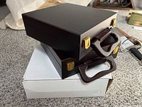 Three poker set cases stacked, two in dark brown wooden briefcases with gold hinges and handles, one in white packaging box underneath