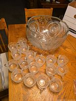 Full view of the glass punch bowl and 17 glass cups arranged on a wooden table.