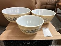 Front view of three nesting Pyrex Homestead mixing bowls showing beige exterior with blue floral pattern and white interior.
