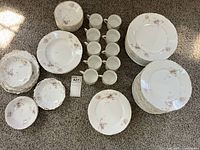 Full lot spread on carpet showing varied China pieces including plates in stacks, bowls, and cups in rows.