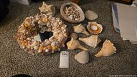 Full display of shell decorated mirror, the abalone shell filled with small shells, large conch shells, sand dollar, and additional shells on carpeted floor.