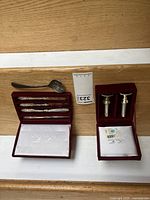 Set of silver plated flatware including four butter spreaders and one soup spoon displayed in a velvet box, alongside their original packaging.