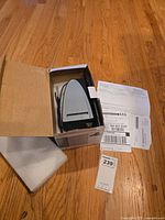 Converter device in its box on a wooden floor with paperwork nearby, viewed from the top showing the device nestled inside packaging.