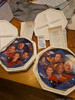 Two vintage Star Trek collectible plates with their white display boxes and informational inserts laid out on a surface.