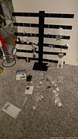 Display of multiple sterling silver pendants and pins hanging on a black display stand with some pieces arranged on the table below, showing about 30+ items in total