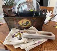 Full view of box with items outside showing napkins, souvenir spoon, cheese server in box, glass plate, and wine rack inside box
