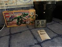 Lot items arranged on blue tiled surface including unopened LEGO box, binocular case, and General Electric clock.