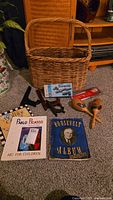 Photo showing the large woven basket, Dragon dominoes box, the Picasso book, Roosevelt album, wooden maracas, and plate holders arranged on carpet floor.