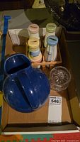 The navy blue ceramic pitcher, crystal condiment dish, and the coin bank milk bottles in a wooden crate shown together in a cardboard box.