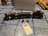 Full view of the metal toy train set showing locomotive, passenger car, caboose, and two small metal parts on blue tile surface.