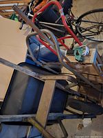 Photo showing wheelbarrow with metal handles and black tray along with dollies, step ladder and tape dispenser.