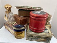 Overall shot of assorted vintage trinket boxes, metal tray, and perfume bottles arranged on a white surface.