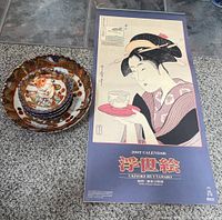 Photo showing the 2007 Ukiyoe By Utamaro calendar depicting traditional Japanese female figure and the stacked serving bowls with a cat figurine on top.