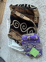 Brown and black tapestry shoulder bag with geometric swirl design and purple quilted Vera Bradley clutch inside a white tray.