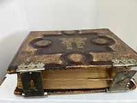 Front angled view of antique leather-bound Bible showing embossed cover, gold tooling, and two metal clasps on the fore-edge.