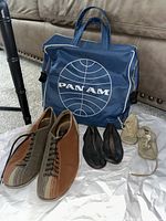 Vintage bowling shoes, Pan Am travel bag, two pairs of leather infant shoes laid out on white paper on carpet.