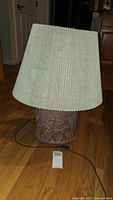Full view of vintage table lamp with ceramic base and fabric shade on wooden floor.