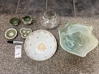 Overview image showing Wedgwood jasperware dishes and cups alongside a Royal Limoges porcelain bowl, a small clear glass vase, and a green blown glass bowl with sculptural edges.